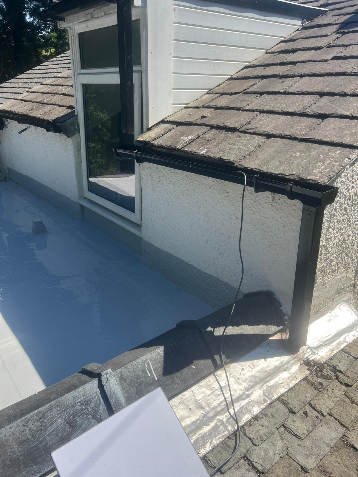 New flat roof or GRP section with Velux skylight viewed from above on a sunny day with green garden beyond