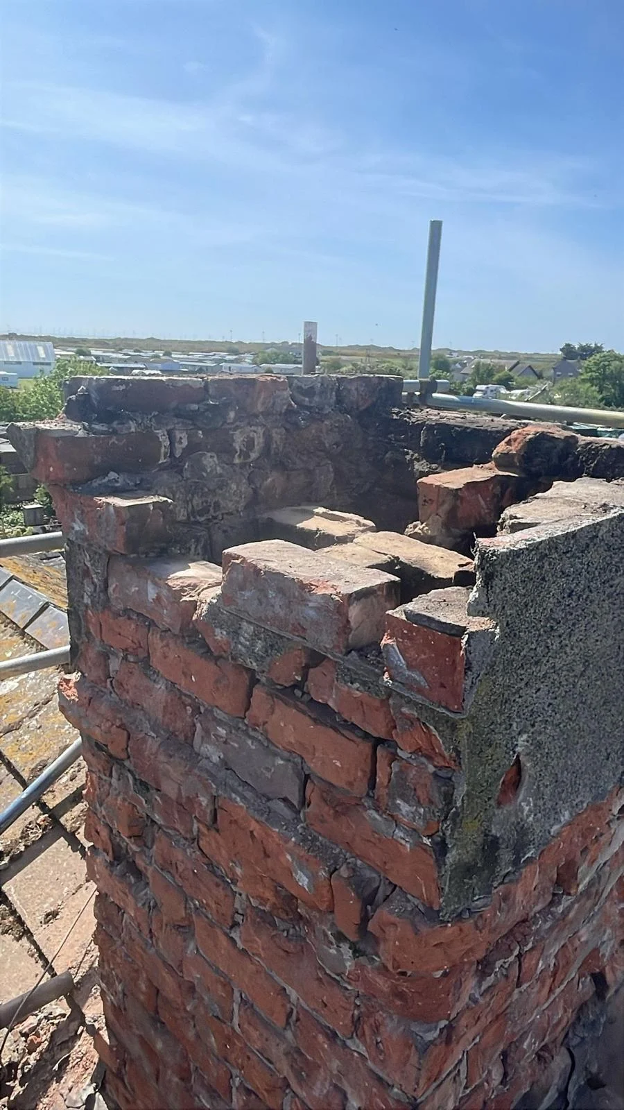 Severely deteriorated brick chimney stack with crumbling mortar and failed render before repair in Cumbria