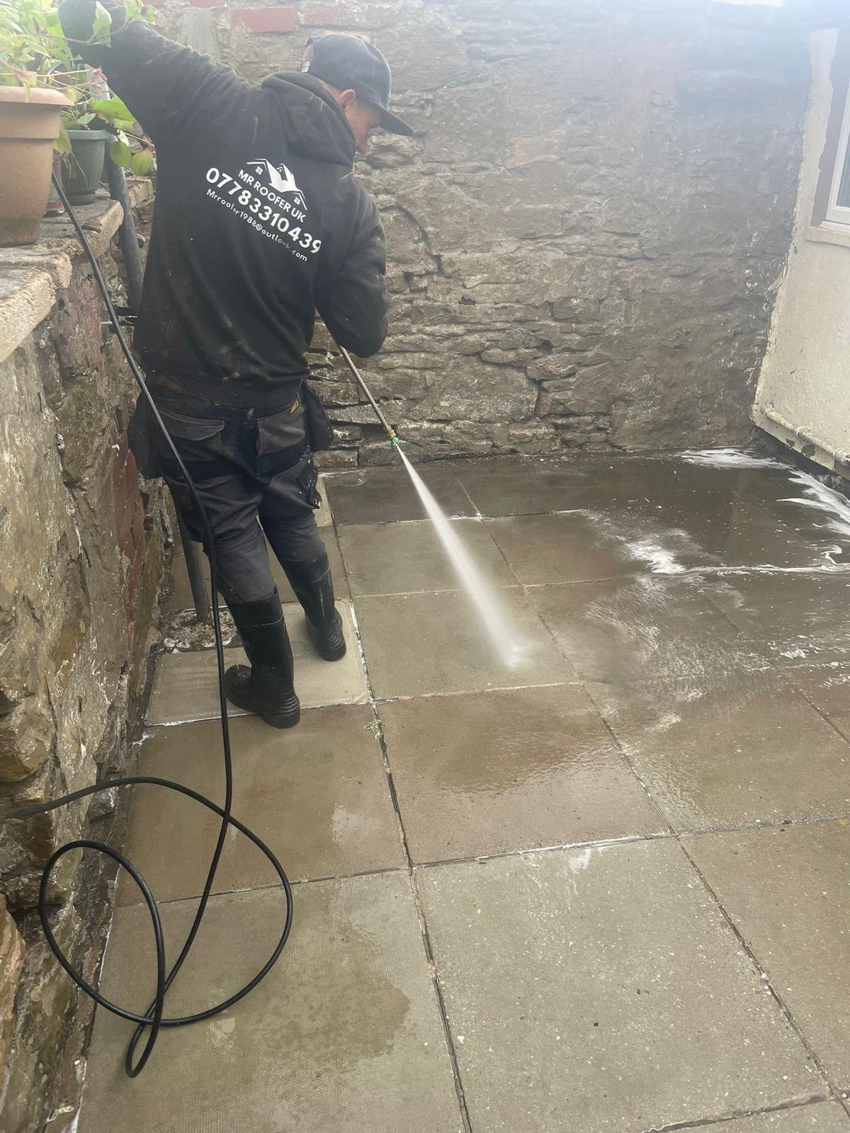 Mr Roofer UK operative in branded workwear using a pressure wash lance to clean a flagstone path between stone boundary walls