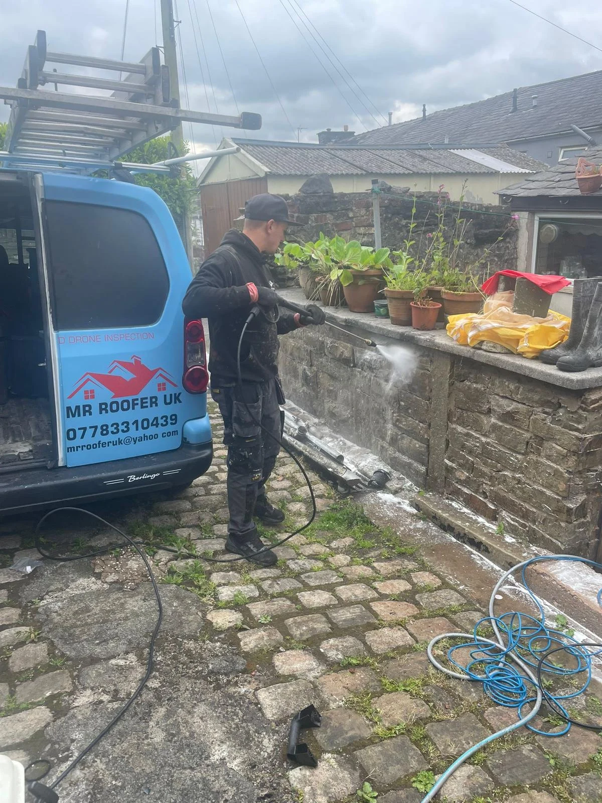 Mr Roofer UK operative soft washing an exterior stone wall beside the company van